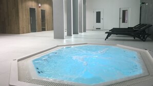 A modern indoor pool area with a central hot tub, lounge chairs, and a wooden wall. - Focus Hotel Premium Lublin Conference & SPA (gmina Jastków)