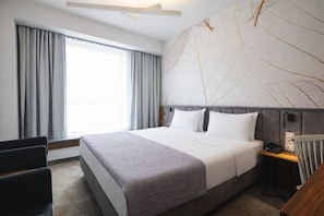 Ett hotellrum med en stor säng, ett skrivbord, en stol och ett fönster med gardiner.