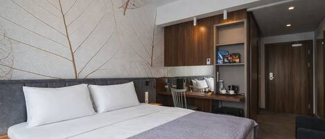 Una habitación de hotel con cama, escritorio, silla, cafetera y estante con artículos de tocador.