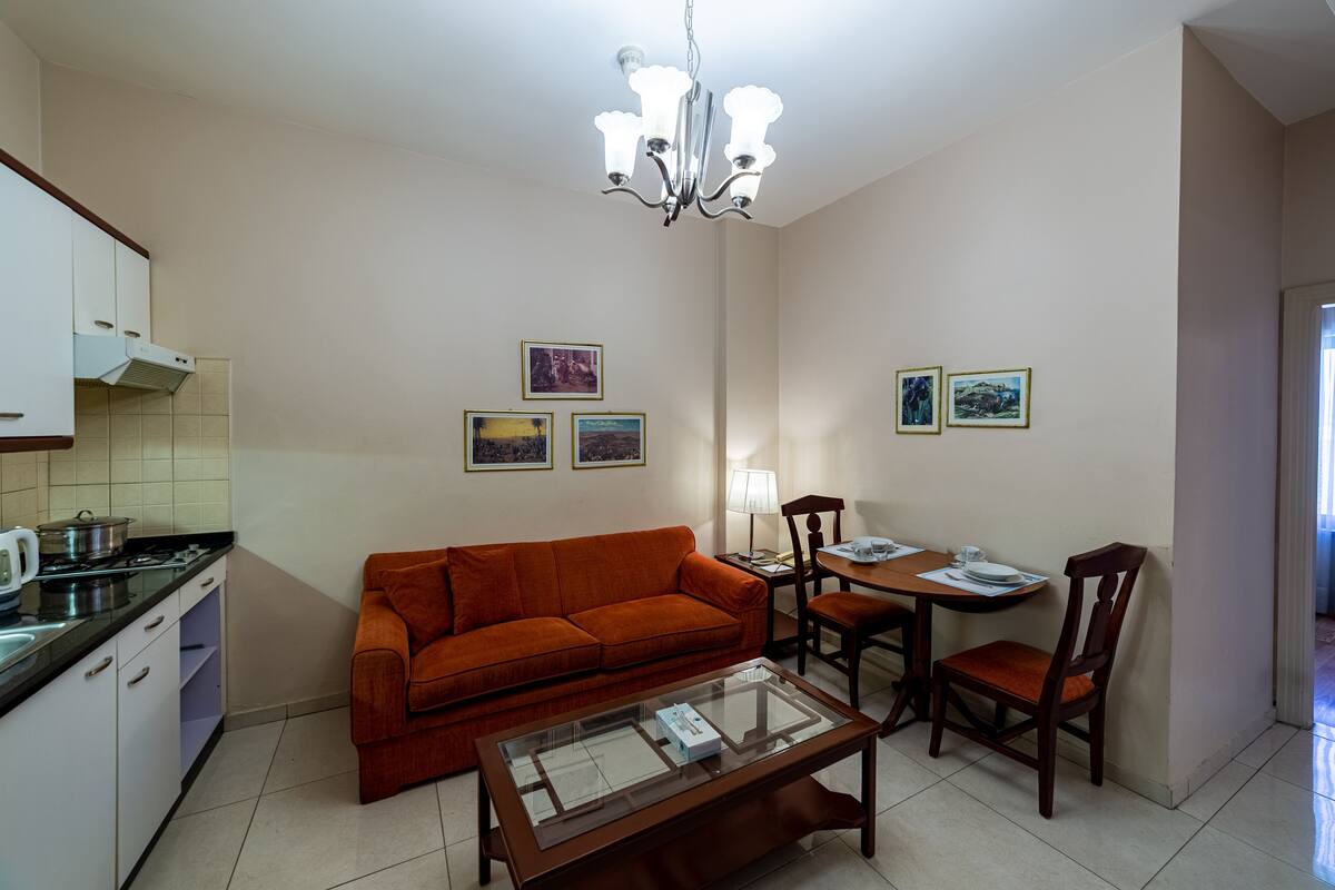 A compact living space with a kitchenette, a sofa, a dining table with chairs, and a chandelier.