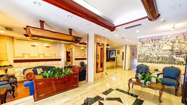 A lobby with a reception desk, seating area, and a mural of a cityscape. - Comfort Hotel Suites (Amman)