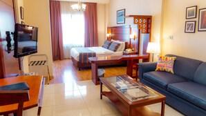 A hotel room with a bed, a sofa, a TV, a coffee table, and a desk. - Comfort Hotel Suites (Amman)