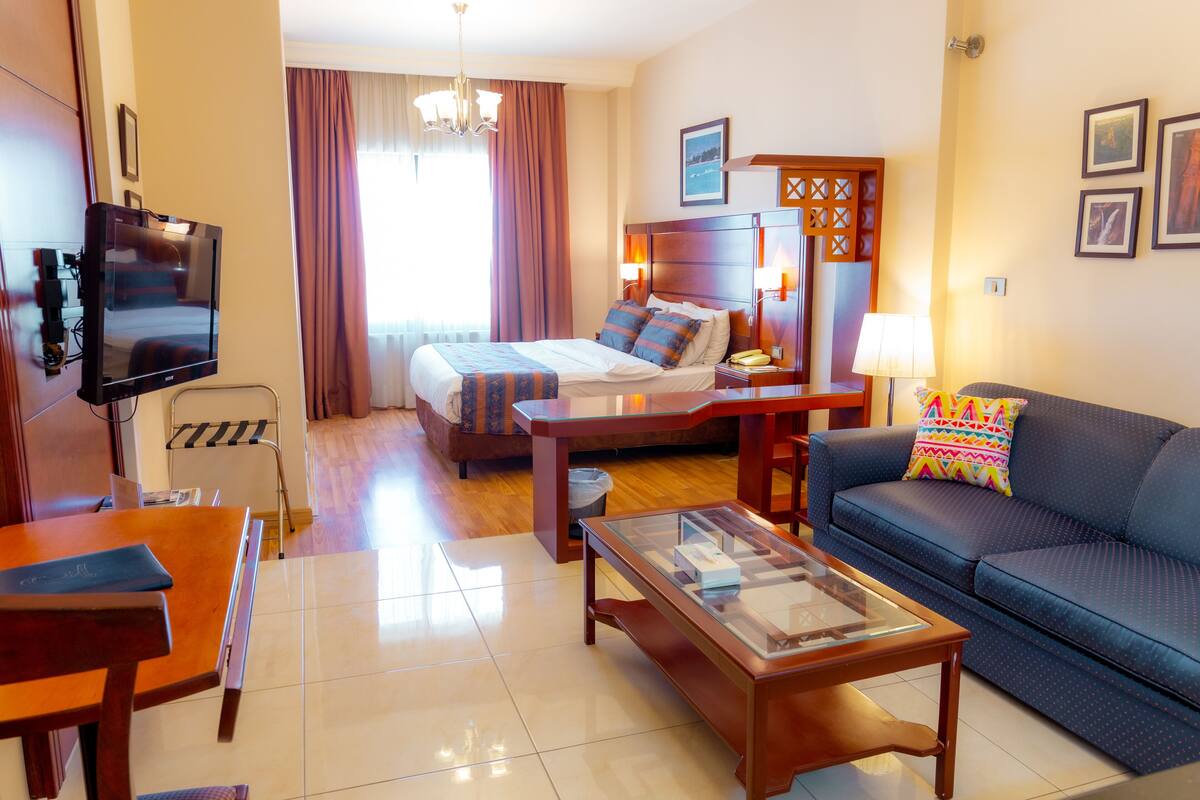 A hotel room with a bed, a sofa, a TV, a coffee table, and a desk.