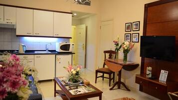 A modern living room with a dining area, a kitchen with white cabinets, a microwave, and a flat-screen TV.