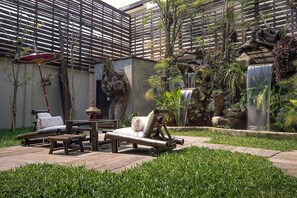 Un jardín con cascada, sillones de descanso y una pérgola.