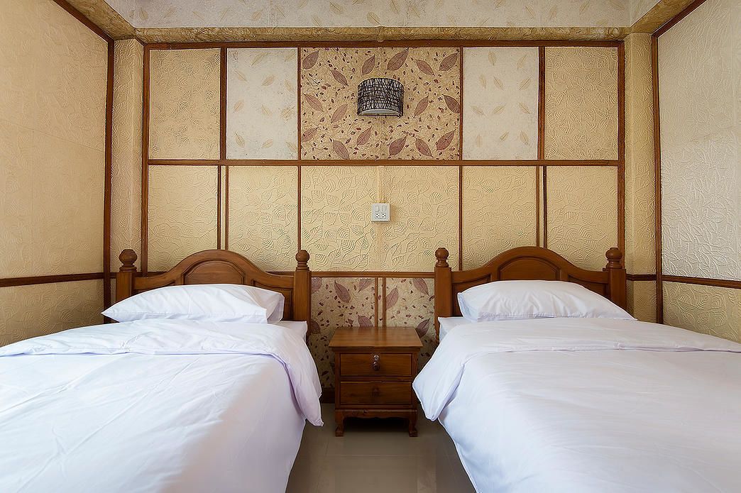 A room with two beds, wooden headboards, a nightstand, and a decorative wall panel.