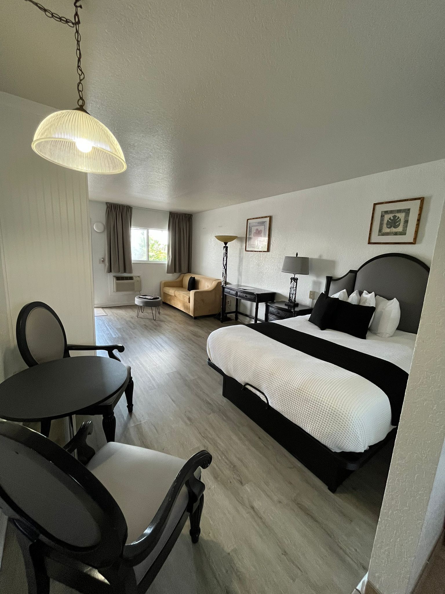 A hotel room with a bed, a desk, a chair, a sofa, and a hanging light fixture.