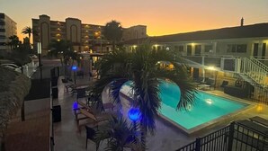A hotel pool area with a sunset view, palm trees, and a staircase leading to the upper floors. - Holiday Isles Resort (Madeira Beach)
