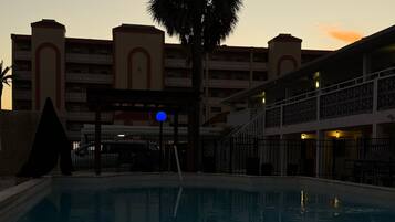 A swimming pool with a palm tree and a building with balconies in the background.