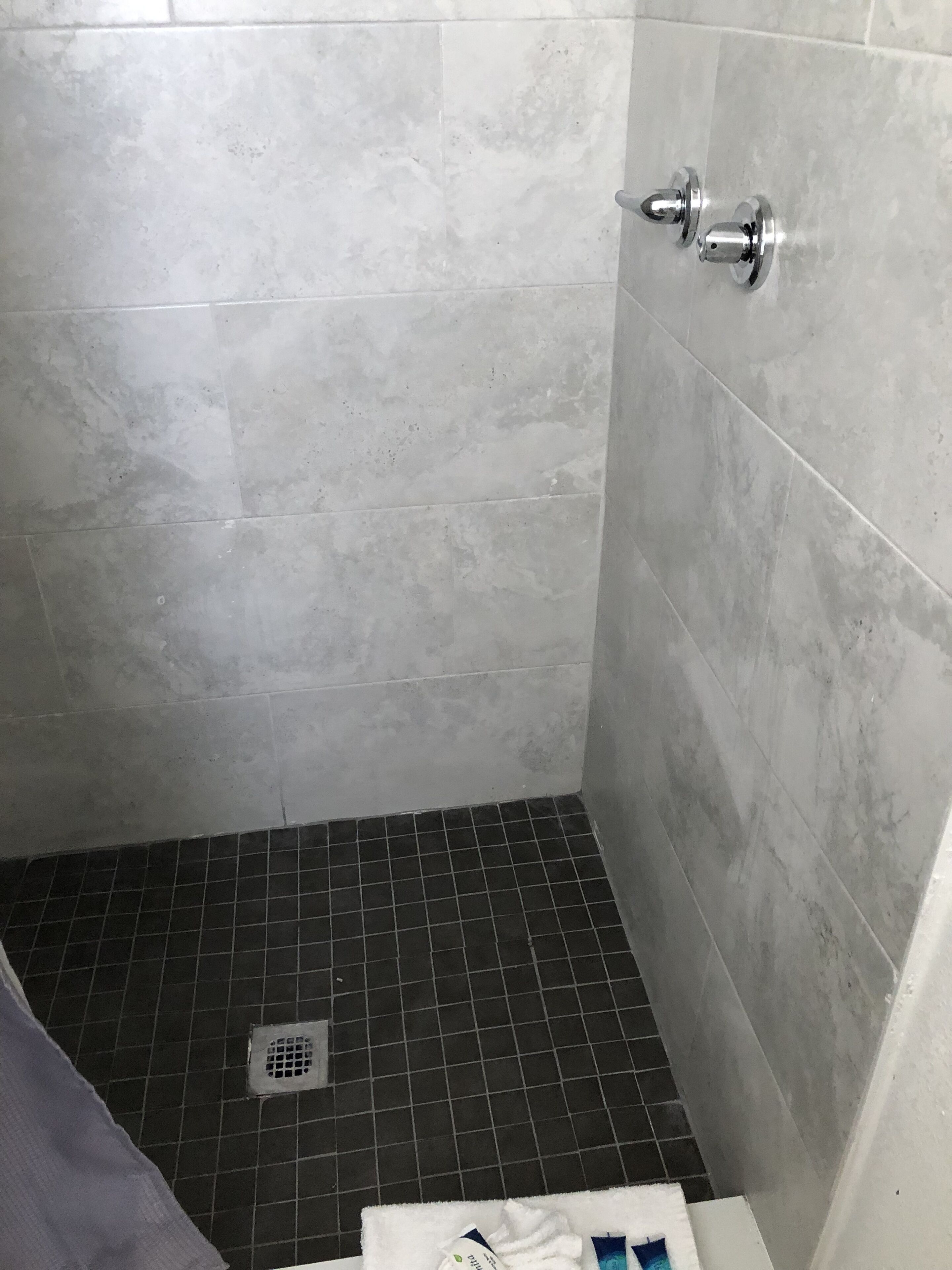 Bagno con pareti rivestite di piastrelle grigie, pavimento in piastrelle nere, zona doccia e porta asciugamani.