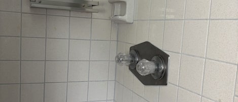 Un baño con paredes de azulejos blancos, un cabezal de ducha y un perchero para toallas.