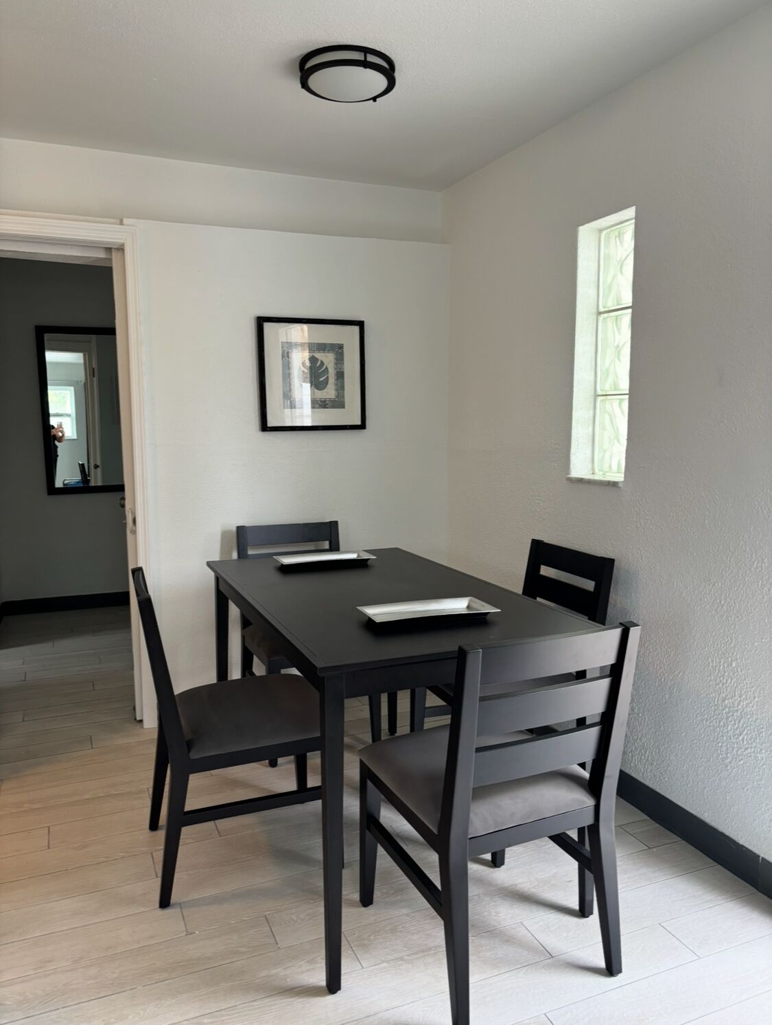 A dining area with a dark wooden table and four chairs, a framed picture on the wall, and a window with a view.