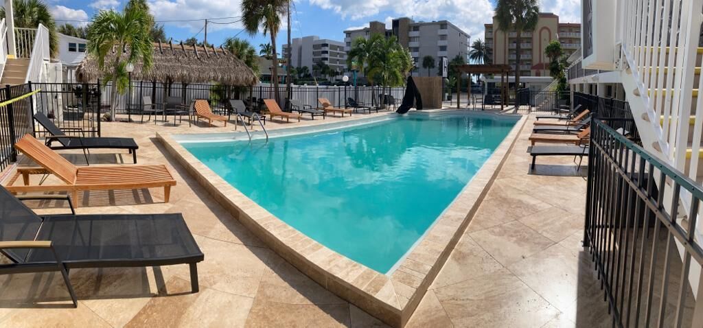 A rectangular swimming pool with lounge chairs and a thatched-roof structure in the background.