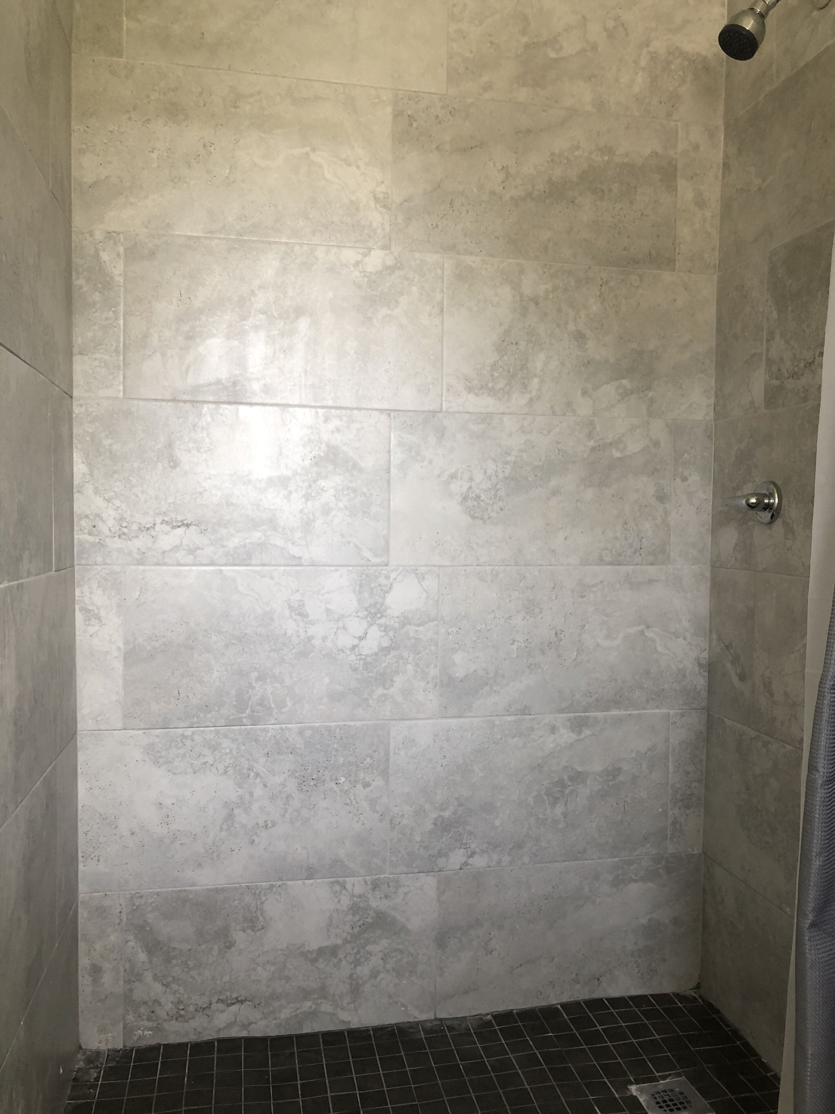 A shower with grey tiles and a metal showerhead.