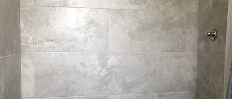 A shower with grey tiles and a metal showerhead.