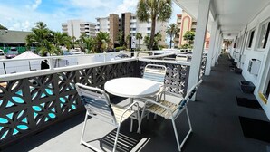 A covered outdoor seating area with a table and chairs, a pool in the background, and buildings around. - Holiday Isles Resort (Madeira Beach)