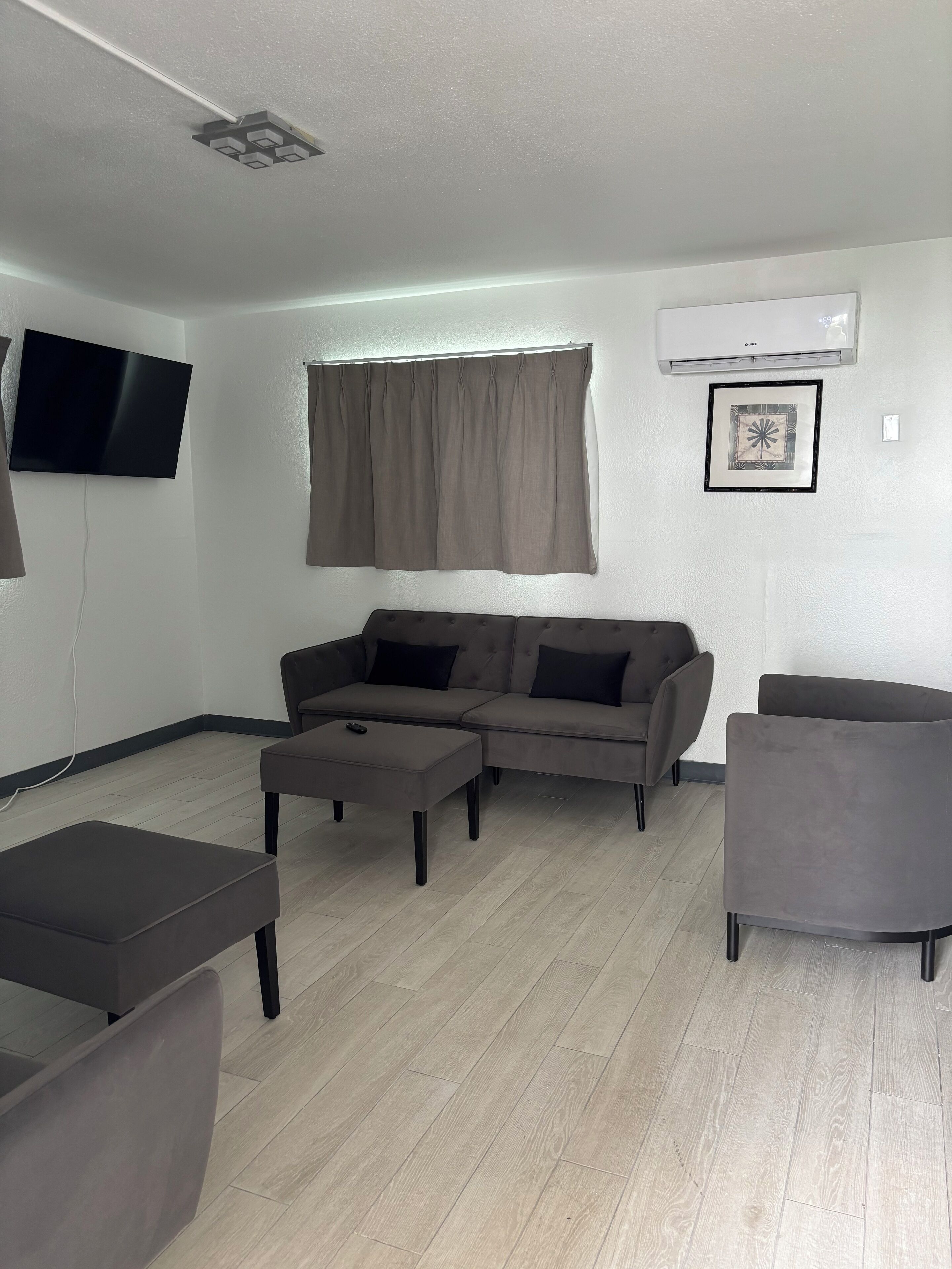 Ein modernes Wohnzimmer mit einem grauen Ecksofa, einem kleinen Hocker, einem grauen Sessel und einem an der Wand befestigten Flachbildfernseher.