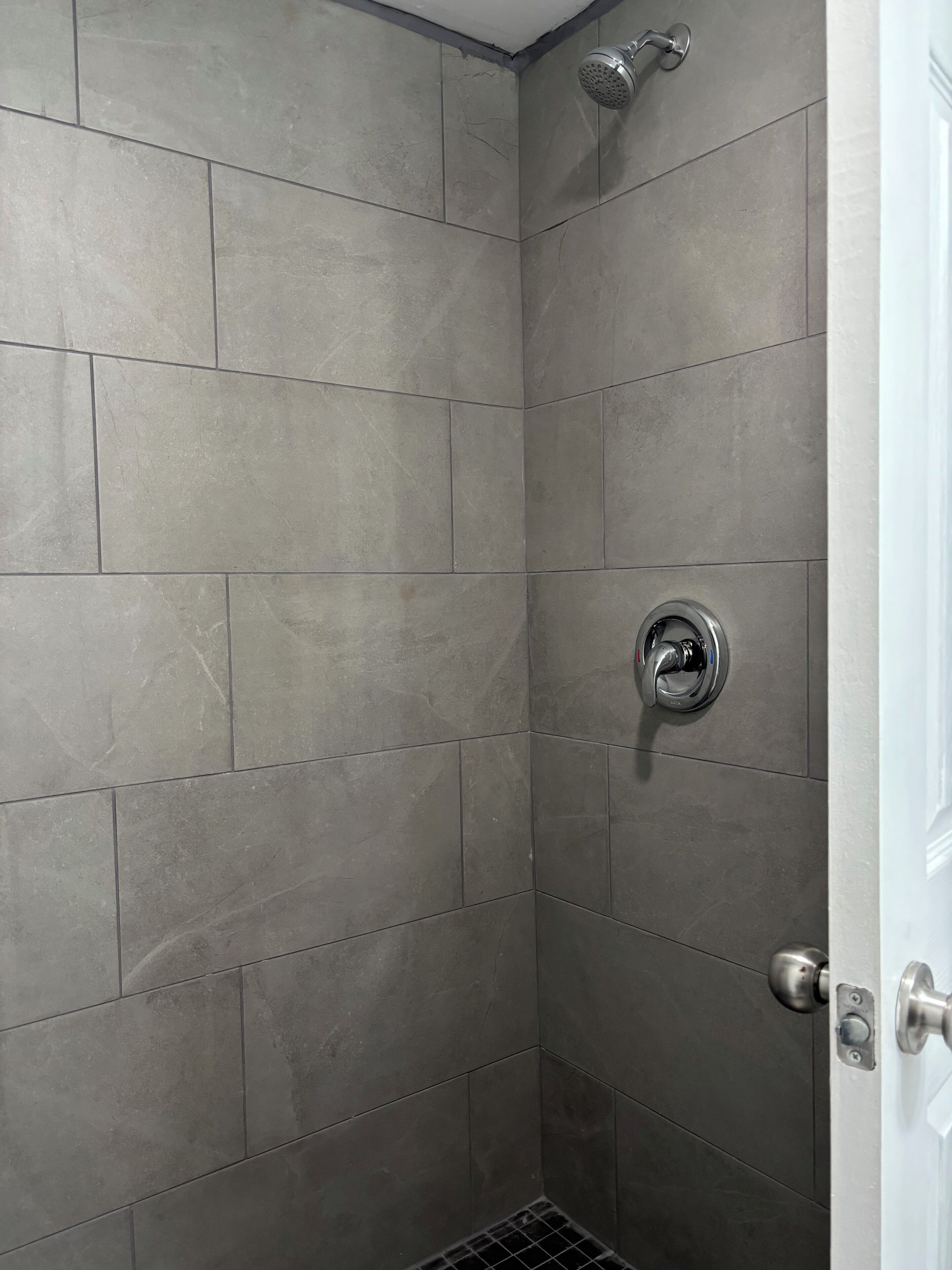 A shower with grey tiles and a modern faucet.