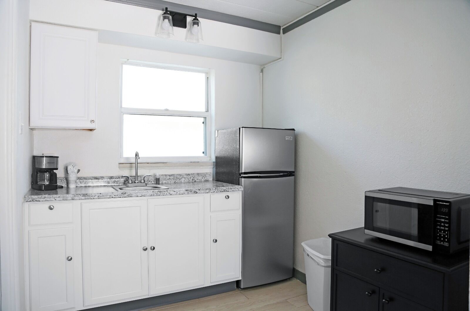 A kitchen with white cabinets, a stainless steel refrigerator, a microwave, and a coffee maker.