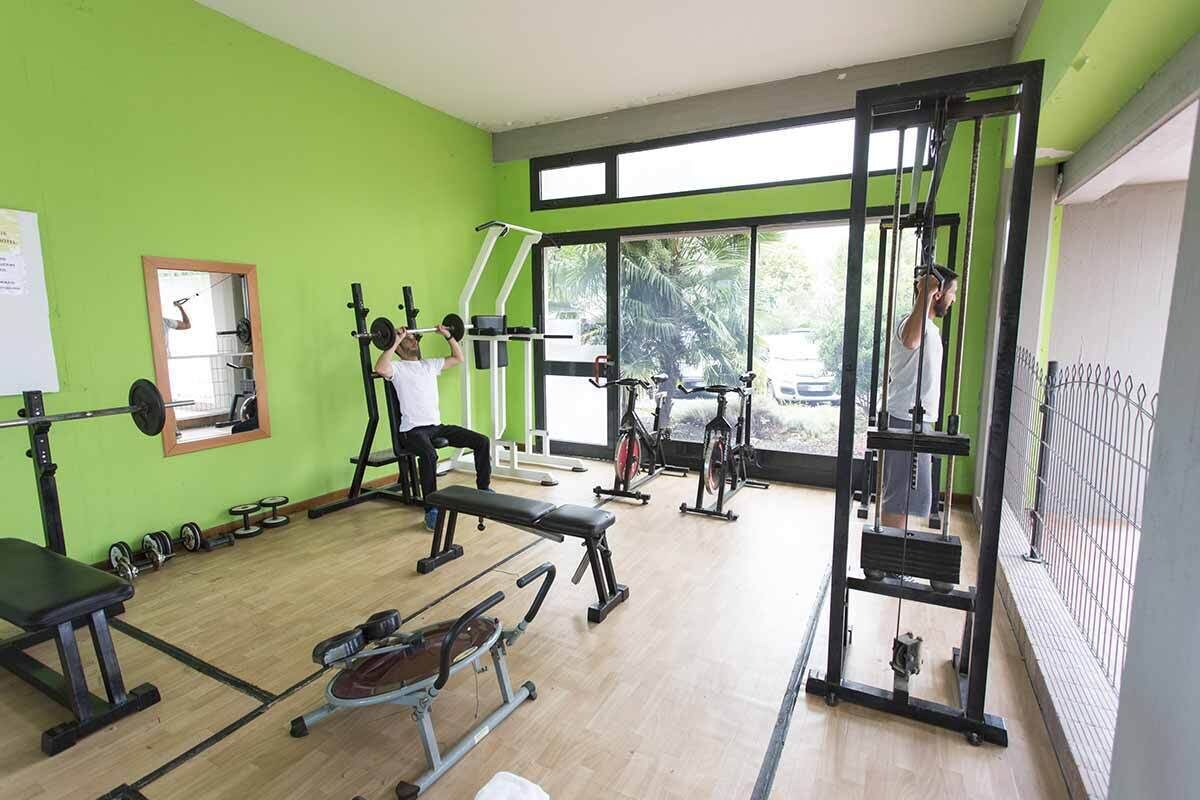Un gimnasio con equipo de ejercicio variado, una banca y un espejo en la pared.