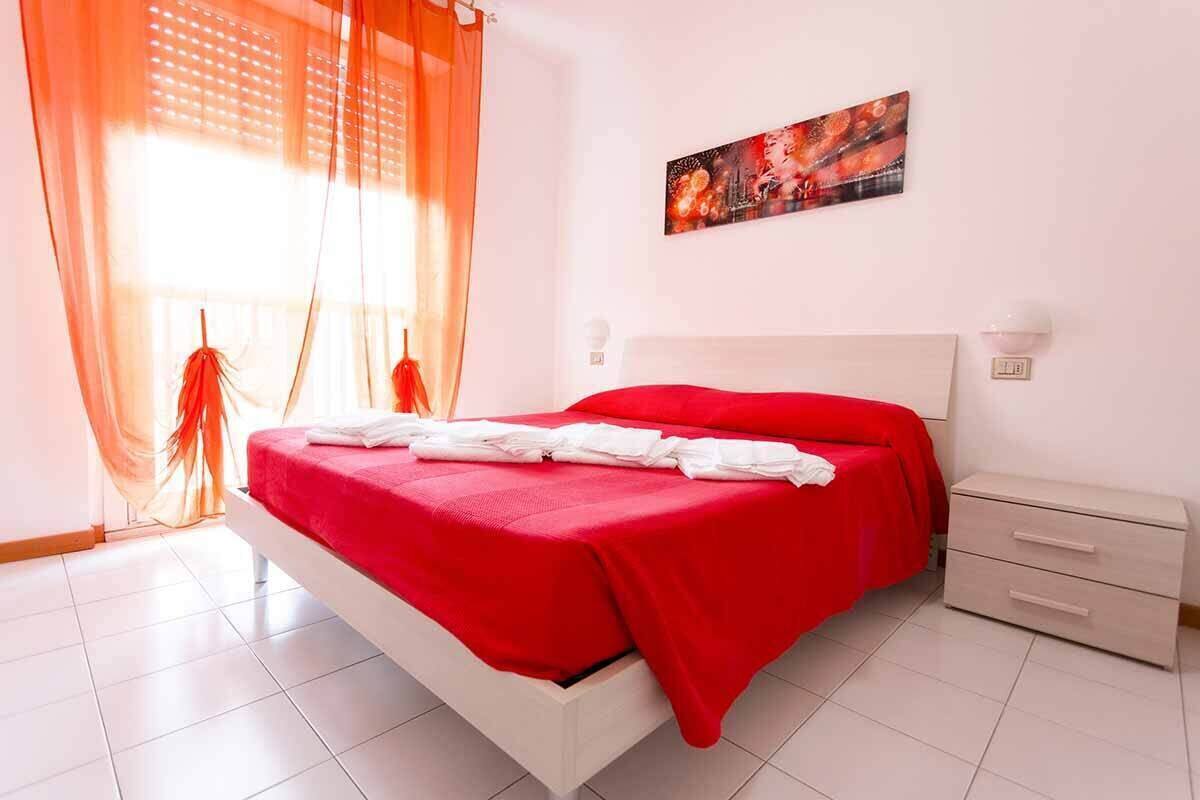 Un dormitorio con una cama blanca, ropa de cama roja, una mesita de noche y un cuadro en la pared.