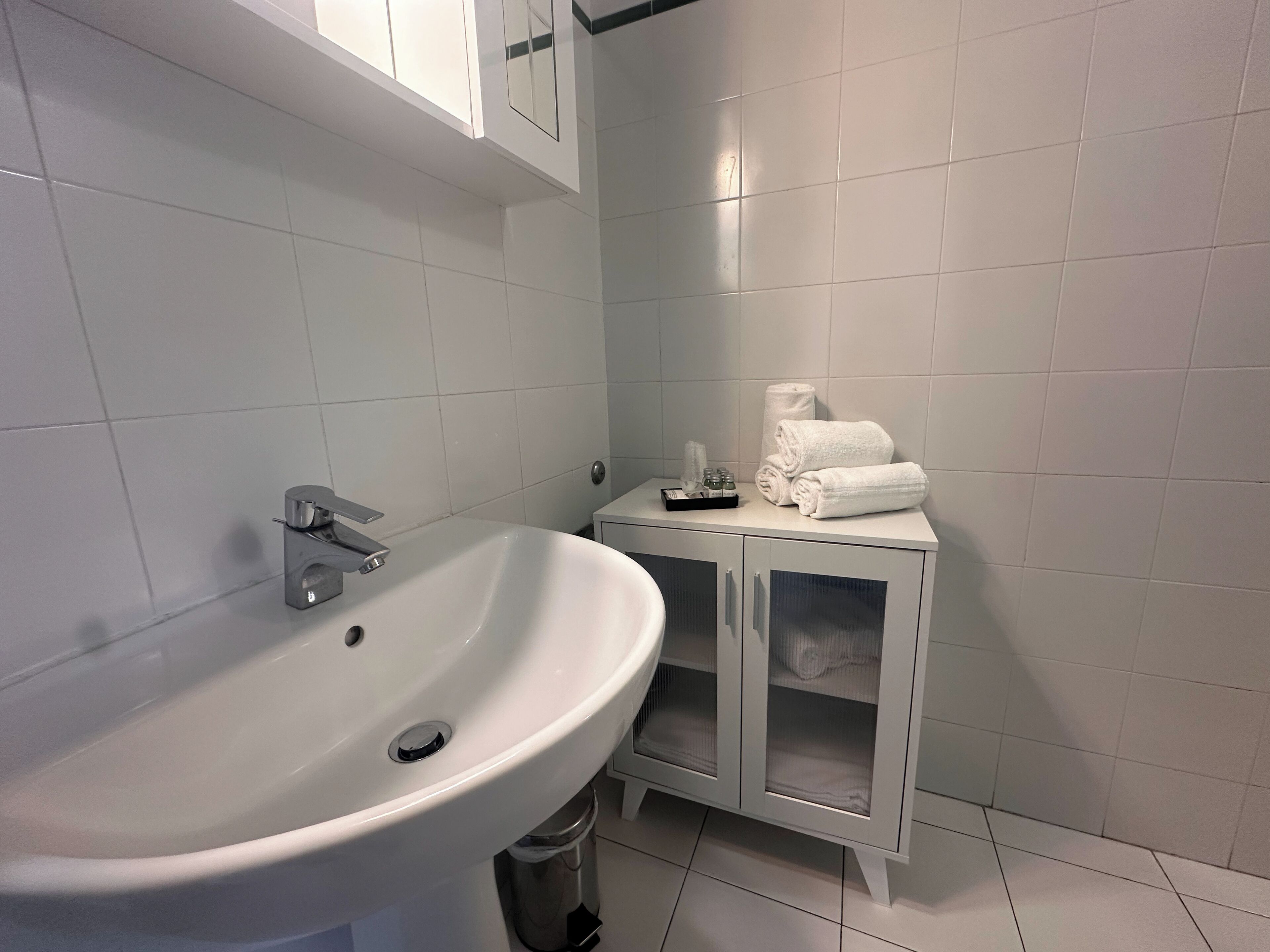A bathroom with a white sink, a mirror, and a cabinet with towels.