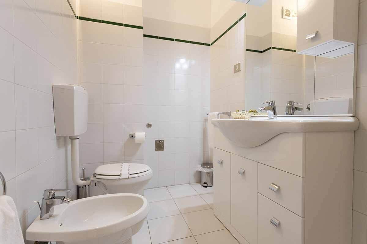 A modern bathroom with white tiles, a toilet, a sink, and a mirror.