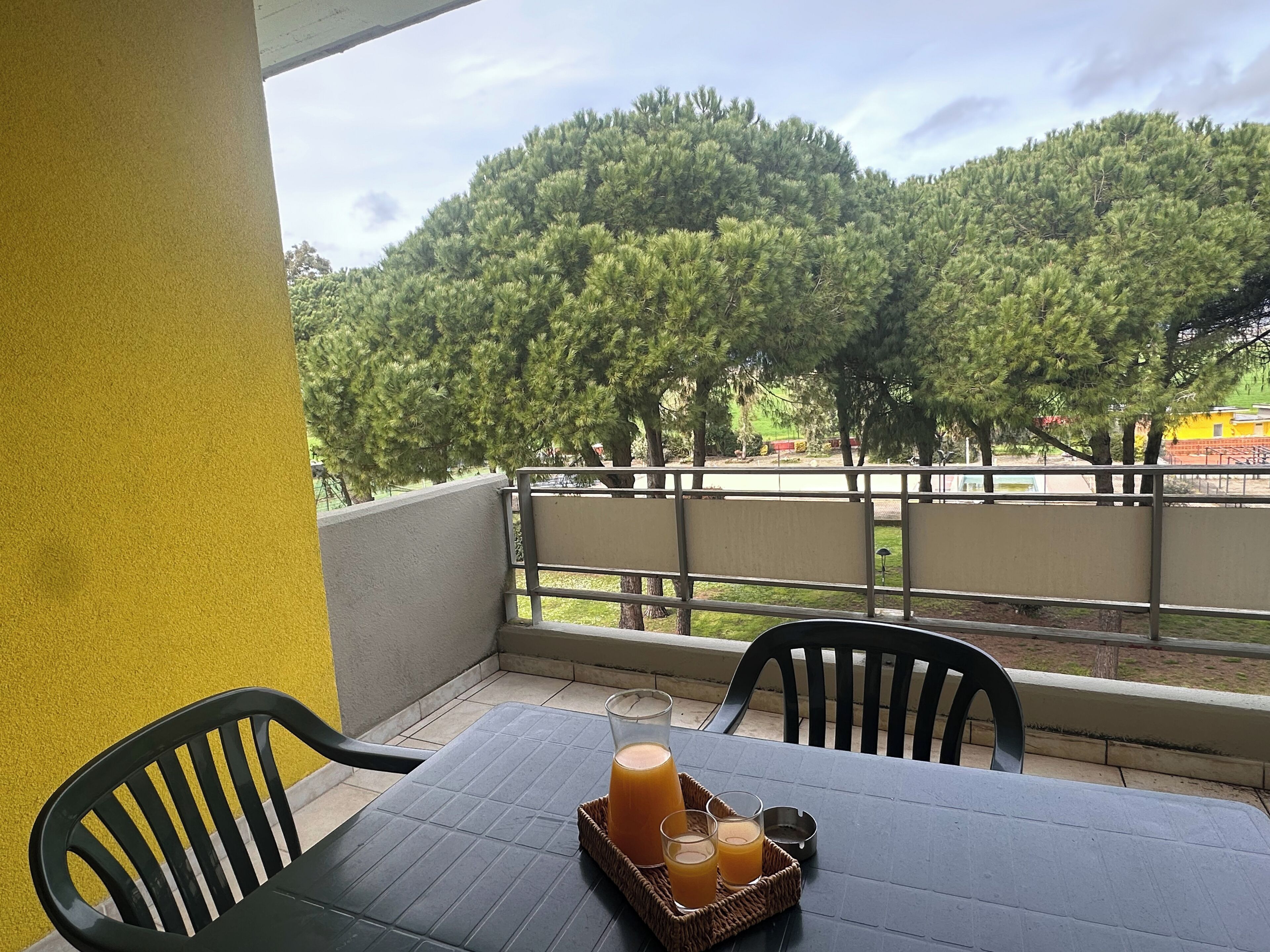 Un balcon avec une table dressée pour deux personnes, agrémenté d’un plateau avec des verres de jus d’orange et une bouteille.