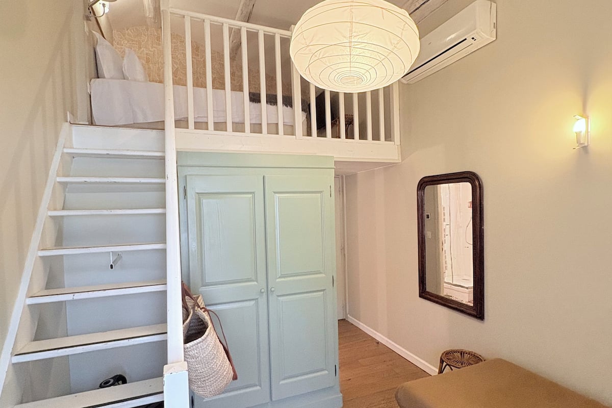 A staircase leading to a loft bedroom with a hanging light fixture, a wardrobe, and a mirror on the wall.