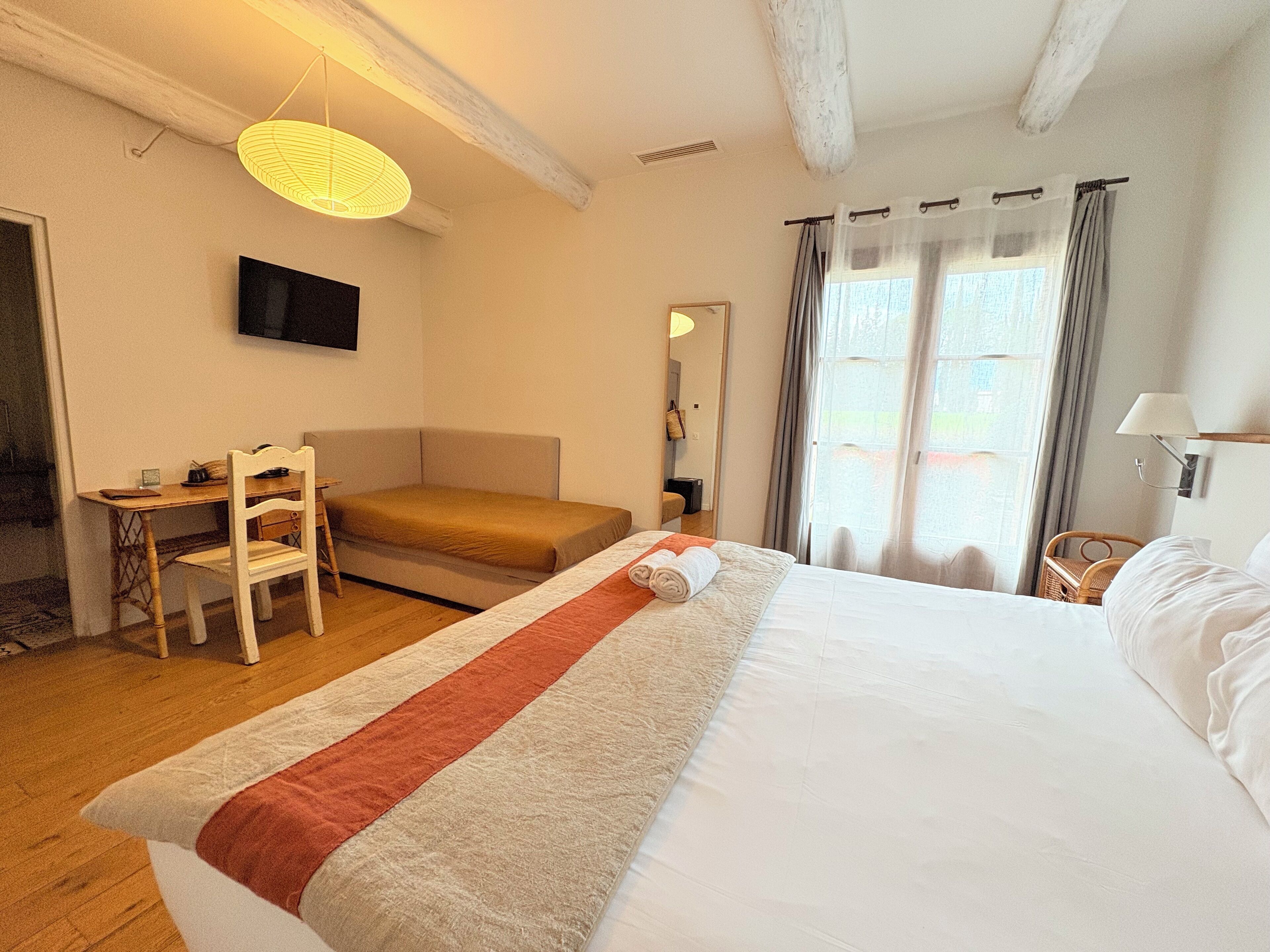 A hotel room with a bed, a desk, a chair, a television, and a window with curtains.