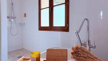 A bathroom with a shower, a sink, a window, and a wooden tray with a yellow container and a wooden block.