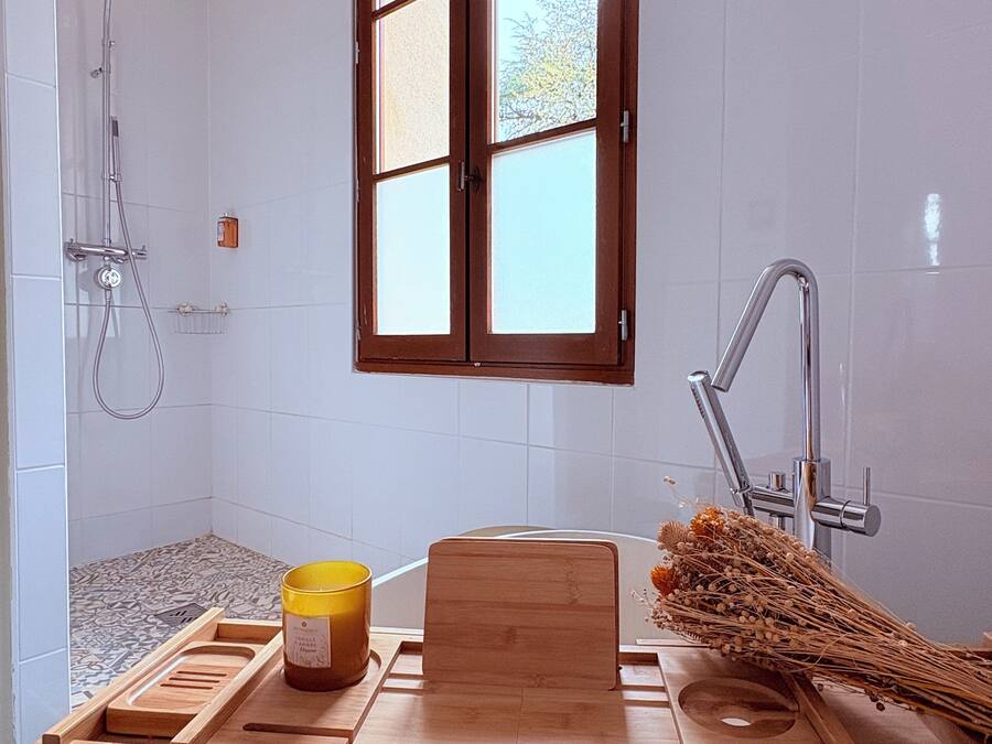A bathroom with a shower, a sink, a window, and a wooden tray with a yellow container and a wooden block.