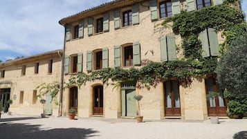 Um edifício com várias janelas, algumas com persianas, e um pátio com plantas em vasos.