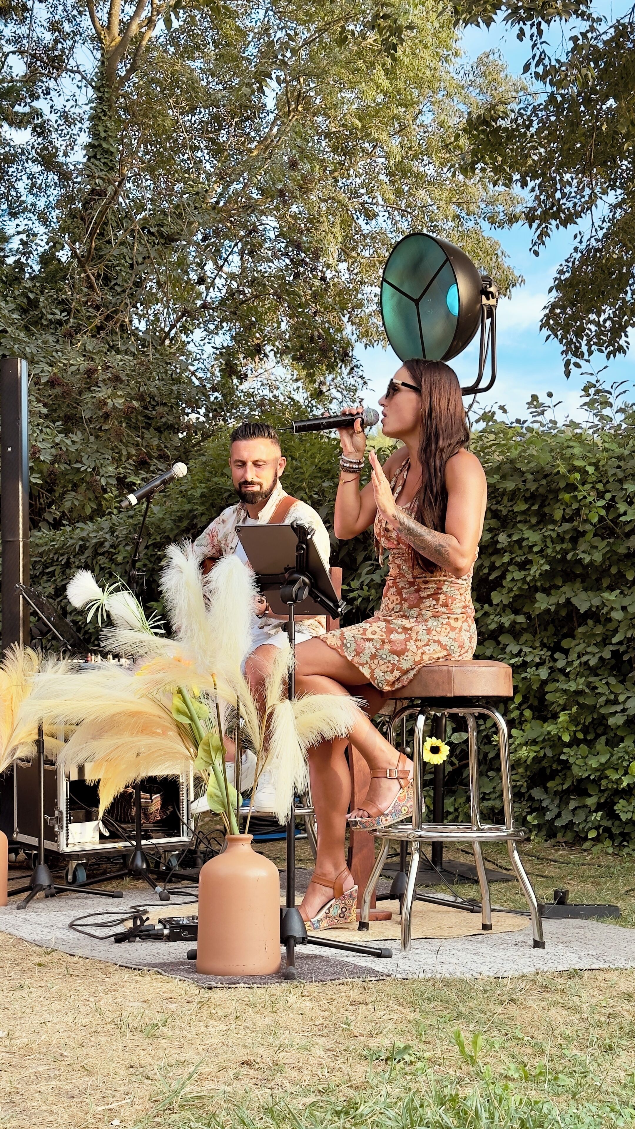 Une personne assise sur un tabouret, un microphone à la main, une autre personne debout à côté d’elle, et un grand haut-parleur à l’arrière-plan.