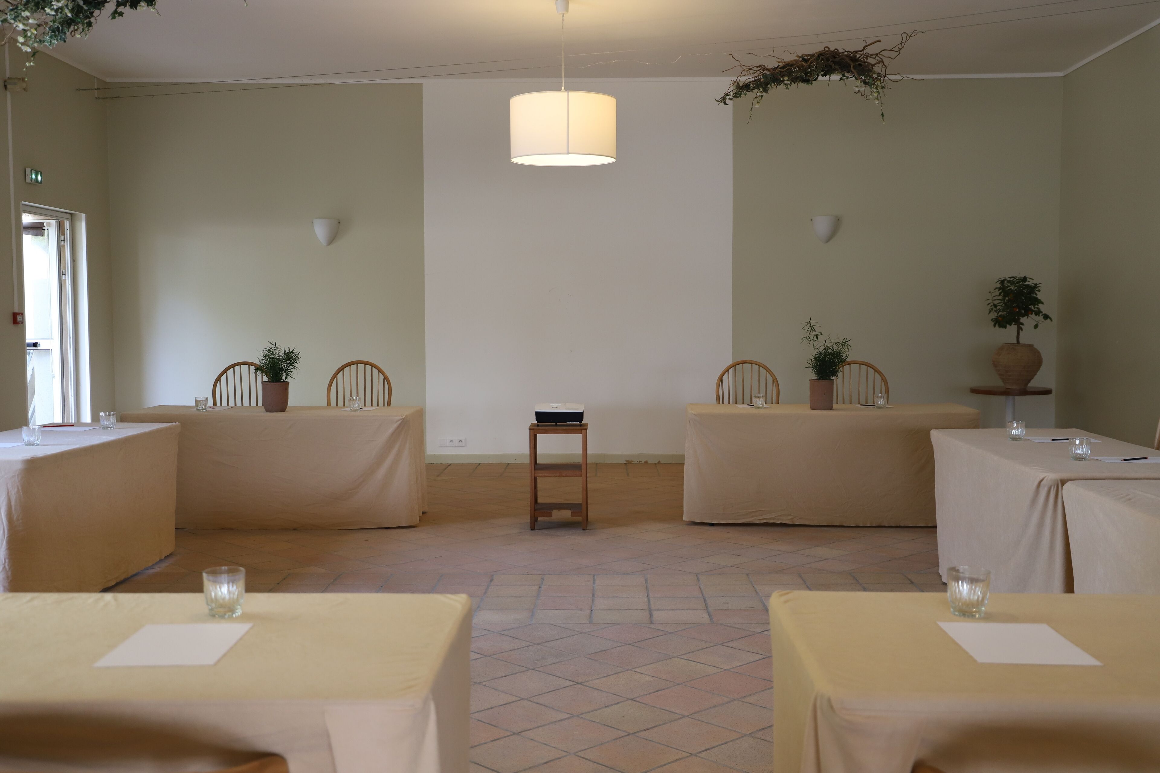 Une pièce comprenant quatre tables, chacune recouverte d’une nappe beige, et une table centrale sur laquelle est posée une petite plante.
