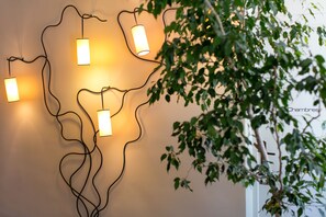 A wall-mounted light fixture with multiple bulbs, a plant with green leaves, and a white door in the background. - Domaine Gao (Aix-en-Provence)