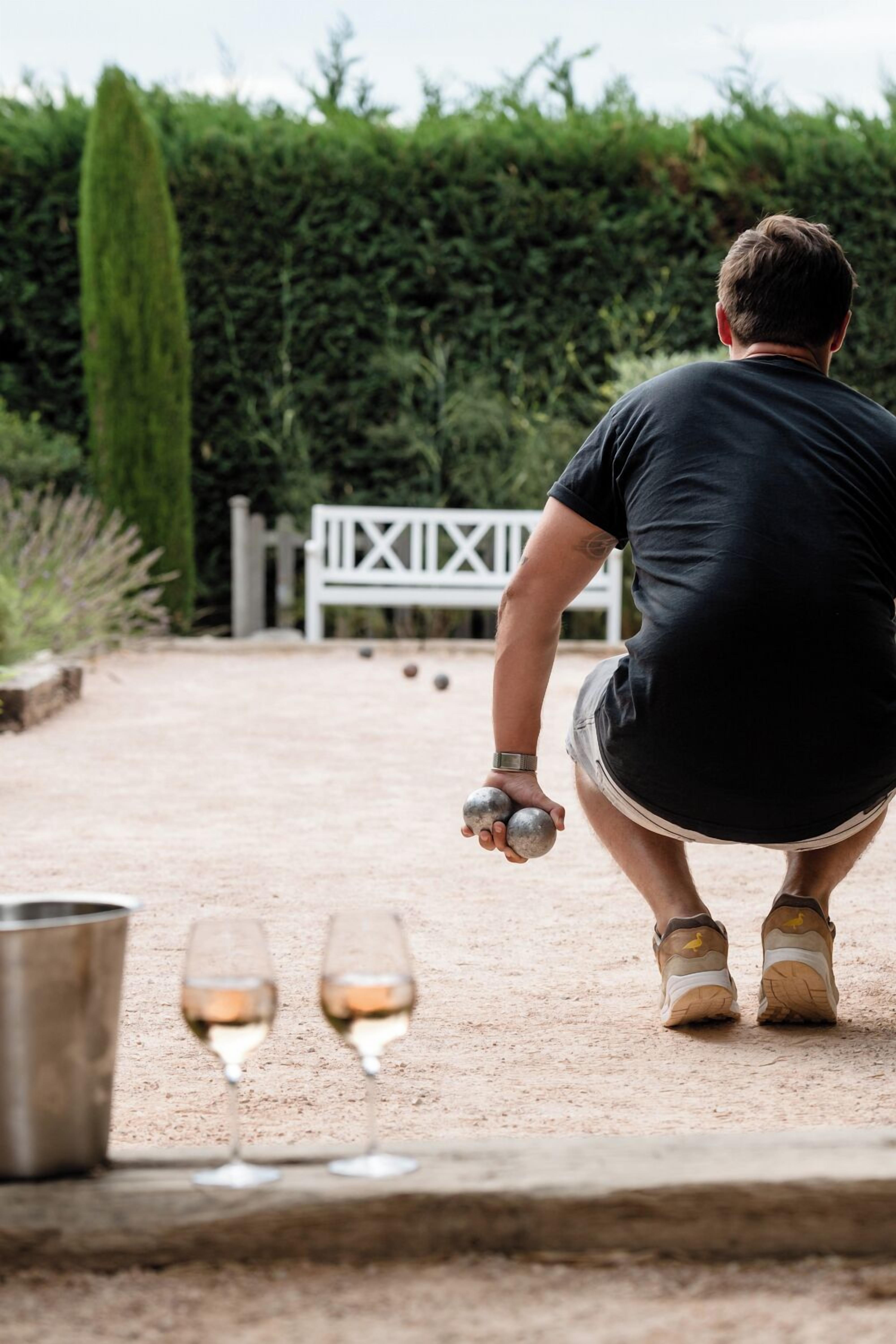 Una persona jugando lawn bowls al aire libre, con una valla blanca y follaje de fondo.