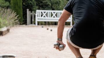 Una persona jugando lawn bowls al aire libre, con una valla blanca y follaje de fondo.