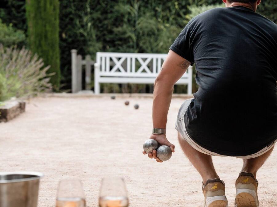 A person playing lawn bowls outdoors with a white fence and greenery in the background.