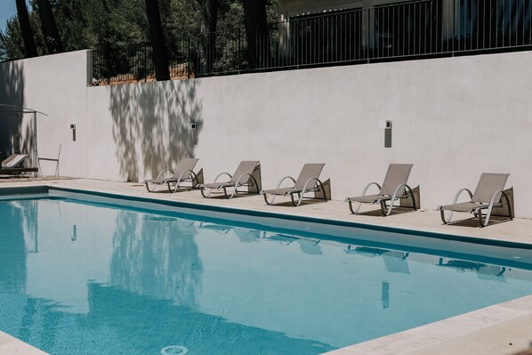 A swimming pool with six sun loungers aligned along the edge, a white wall, and a metal fence in the background. - Domaine Gao (Aix-en-Provence)