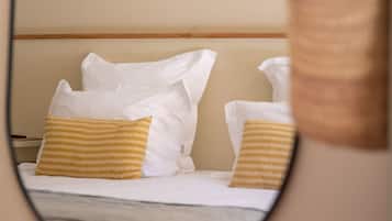 A bed with white bedding and two yellow pillows, a wooden headboard, and a woven basket on the floor.