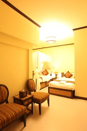 Habitación de hotel con cama, zona de estar con una silla y una mesita, y mesita de noche con lámpara.