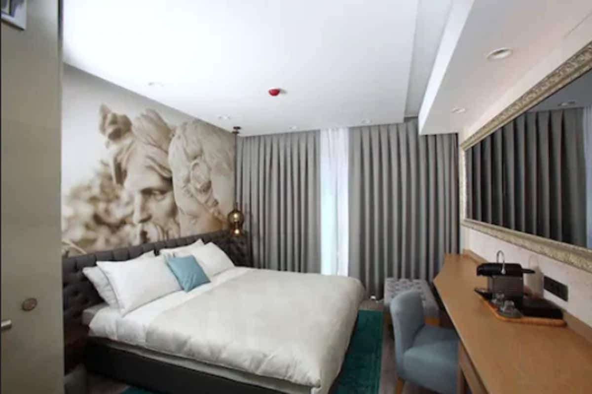 A modern hotel room with a large bed, a desk, and a large mirror.