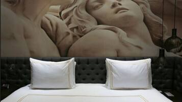 Una cama con sábanas blancas y detalles dorados, un cabecero capitonado y dos almohadas blancas.