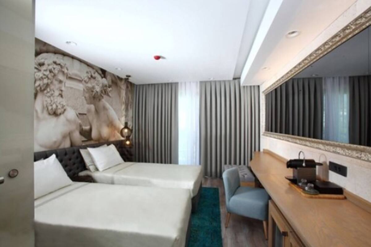 A hotel room with two beds, a desk, a chair, a large mirror, and a decorative wall.