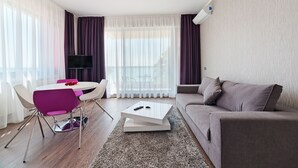 A modern living room with a round dining table, purple chairs, a grey sofa, and a flat-screen TV. - Tomis Garden Apartments (Constanta)