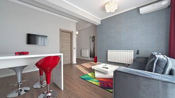 Una sala moderna con un sofá gris, una mesa de centro blanca y un taburete rojo.