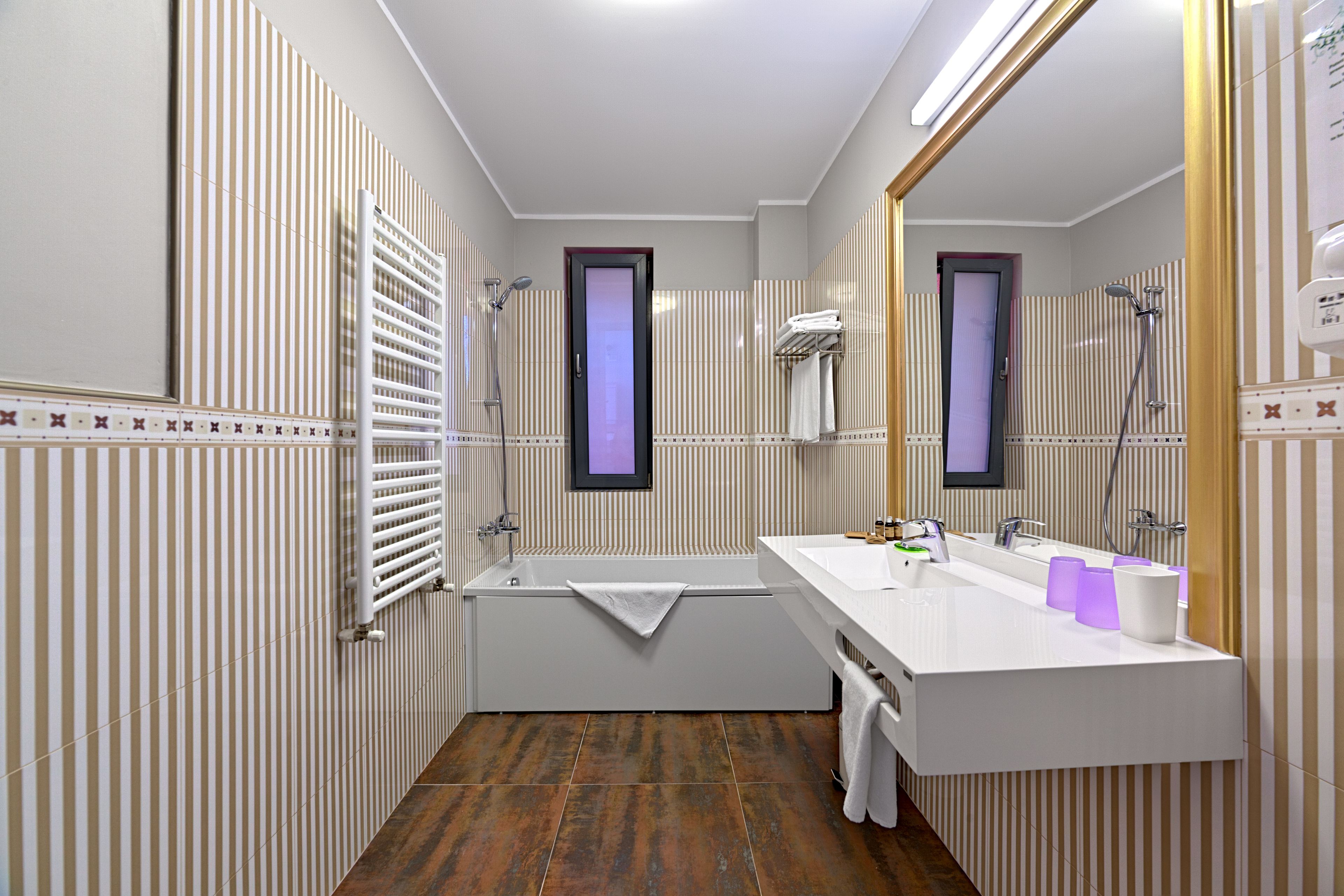 A modern bathroom with a bathtub, a large mirror, and a white sink with purple soap dispensers.