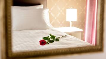A neatly made bed with a white pillow and a single red rose on the bed.