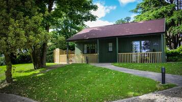 A small building with a green exterior and a dark roof, surrounded by trees and a grassy area.